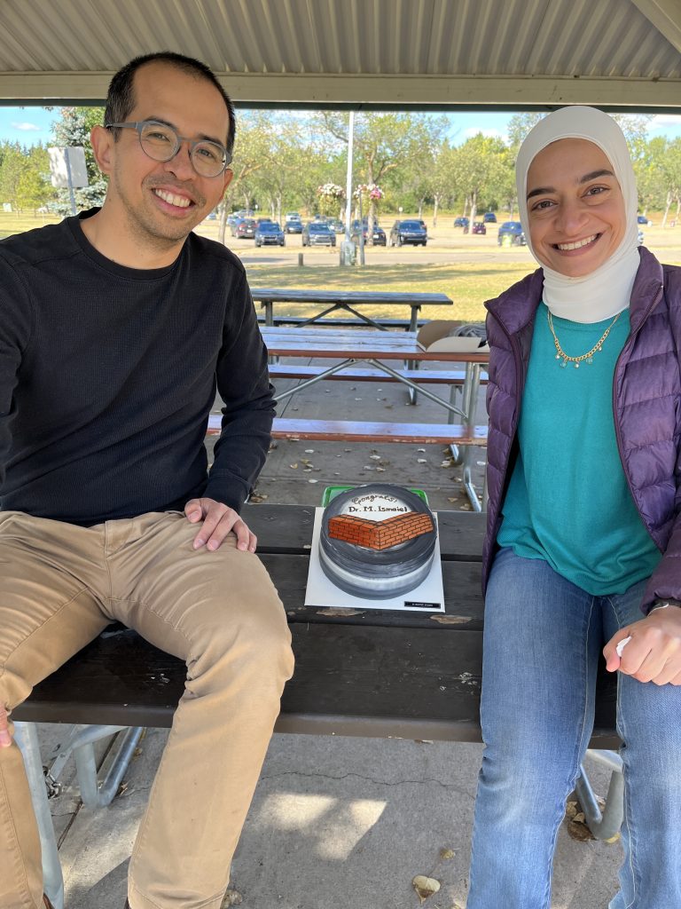 Two group members seated at a picnic table with the celebration cake