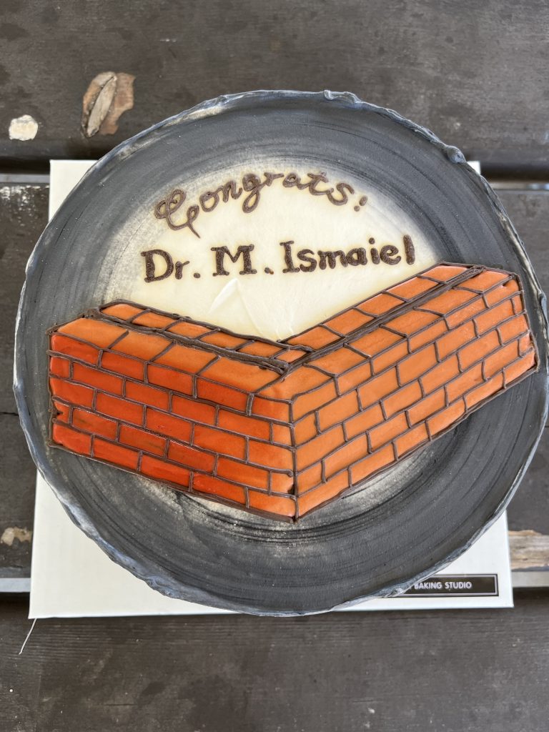 Celebration cake decorated with a brick wall and the words "Congrats! Dr. M. Ismaiel"
