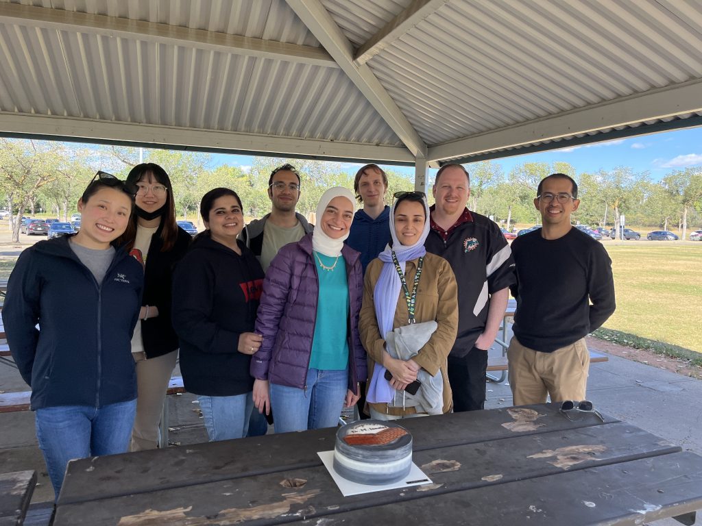Group photo under a picnic shelter, with a celebration cake on the table